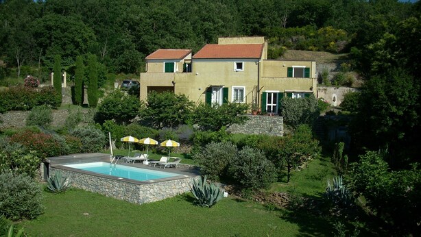 Una casa de dos pisos con piscina, rodeada de abundante vegetación y árboles.
