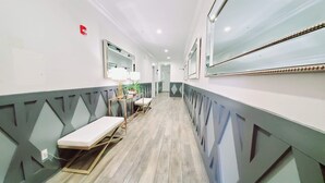 A narrow hallway with a bench, a table with a lamp, and a mirror on the wall.