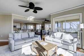 Uma sala de estar espaçosa com dois sofás cinzentos, uma mesa de centro de madeira e uma grande janela com vista para o mar.