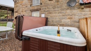 Un bâtiment en pierre doté d’un jacuzzi, d’une antenne parabolique et d’une clôture en bois.