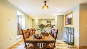 Un coin repas avec une table et des chaises en bois, un luminaire suspendu et une vue sur la cuisine.