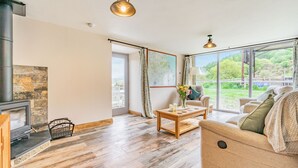 Un salon spacieux doté d’une cheminée, de grandes fenêtres et offrant une vue sur la verdure.