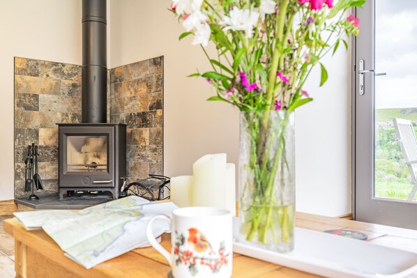 A cozy room with a fireplace, a wooden table with a map, a mug, and a vase with flowers.