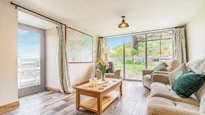Un salon spacieux avec une table basse en bois, un canapé beige et une grande fenêtre donnant sur l’extérieur.