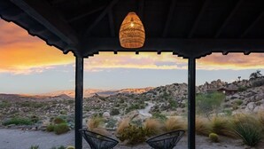 Ein überdachter Außenbereich mit Sitzgelegenheit für zwei Personen, einer hängenden Lampe und Blick auf eine Wüstenlandschaft.