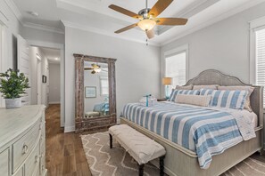 A bedroom with a bed, a ceiling fan, a dresser, a mirror, and a plant.