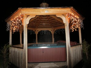 Relax in a serene hot tub surrounded by a wooden bench under a gazebo.