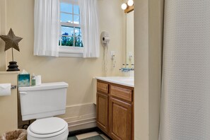 Une salle de bain comprenant des toilettes, un meuble-lavabo avec un miroir, une fenêtre avec des rideaux et une décoration en forme d’étoile sur le mur.