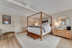 Un lit à baldaquin avec un cadre en bois, une table de chevet avec une lampe, une commode avec des tiroirs et un tableau encadré accroché au mur.