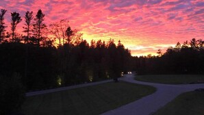 Auringonlasku metsäisen alueen yllä, näköalana mutkitteleva tie.