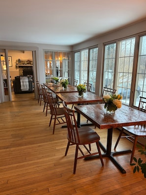 A dining area with a long wooden table, multiple chairs, and large windows. - Lucy Queen Suite in Main House - Red Clover Inn (Mendon)