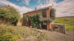 A rustic brick house with ivy-covered walls, a gravel driveway, and a view of the countryside. - Host & Stay | The Red Brick Barn (Rookhope)