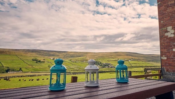 A wooden table with three lanterns on a balcony overlooking a green landscape. - Host & Stay | The Red Brick Barn (Rookhope)