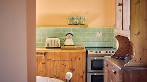 A kitchen with wooden cabinets, a green tiled backsplash, a vintage toaster, and a stove. - Host & Stay | The Red Brick Barn (Rookhope)