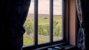 A window with a view of a green landscape, curtains, and a small table with a tray. - Host & Stay | The Red Brick Barn (Rookhope)