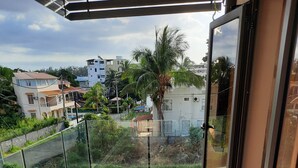 Un balcón con barandilla de vidrio, suelo de baldosas y vistas a edificios y vegetación circundantes.