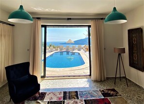 Habitación con vistas a una piscina y mobiliario exterior, un ventanal grande y suelo con baldosas estampadas.
