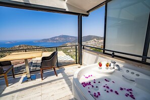 A balcony with a view of the sea, a hot tub with rose petals, and a table with chairs. - Sultan Hotel Kalkan (Kalkan)
