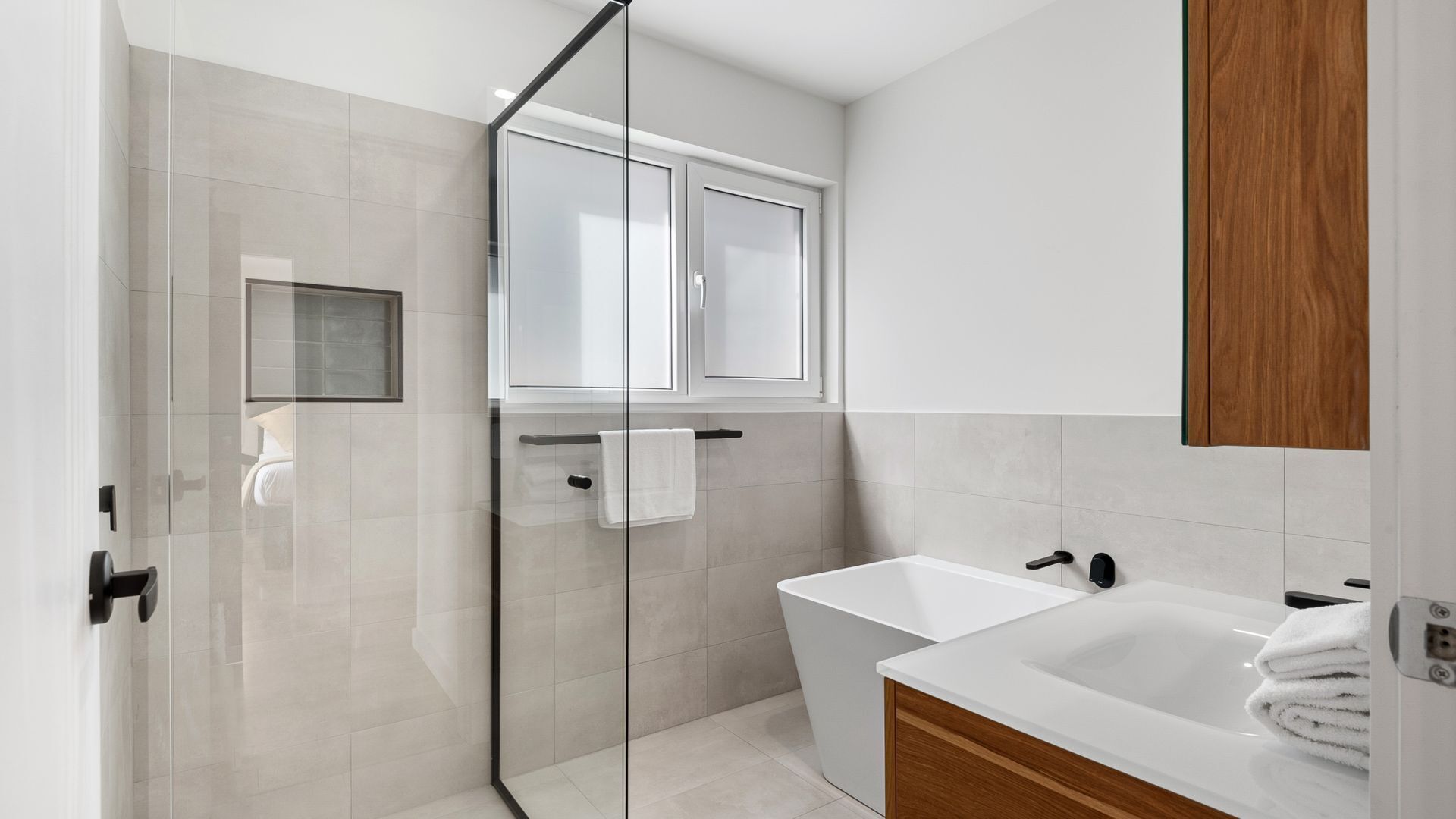 Een moderne badkamer met een douchecabine van glas, een witte badkuip en een houten kast.