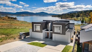 A modern two-story house with a flat roof, large windows, and a view of a lake and mountains. - Lake Villavista - 4BR Luxury Townhouse l Pet Friendly l Lake Views l WiFi l BBQ (East Jindabyne)