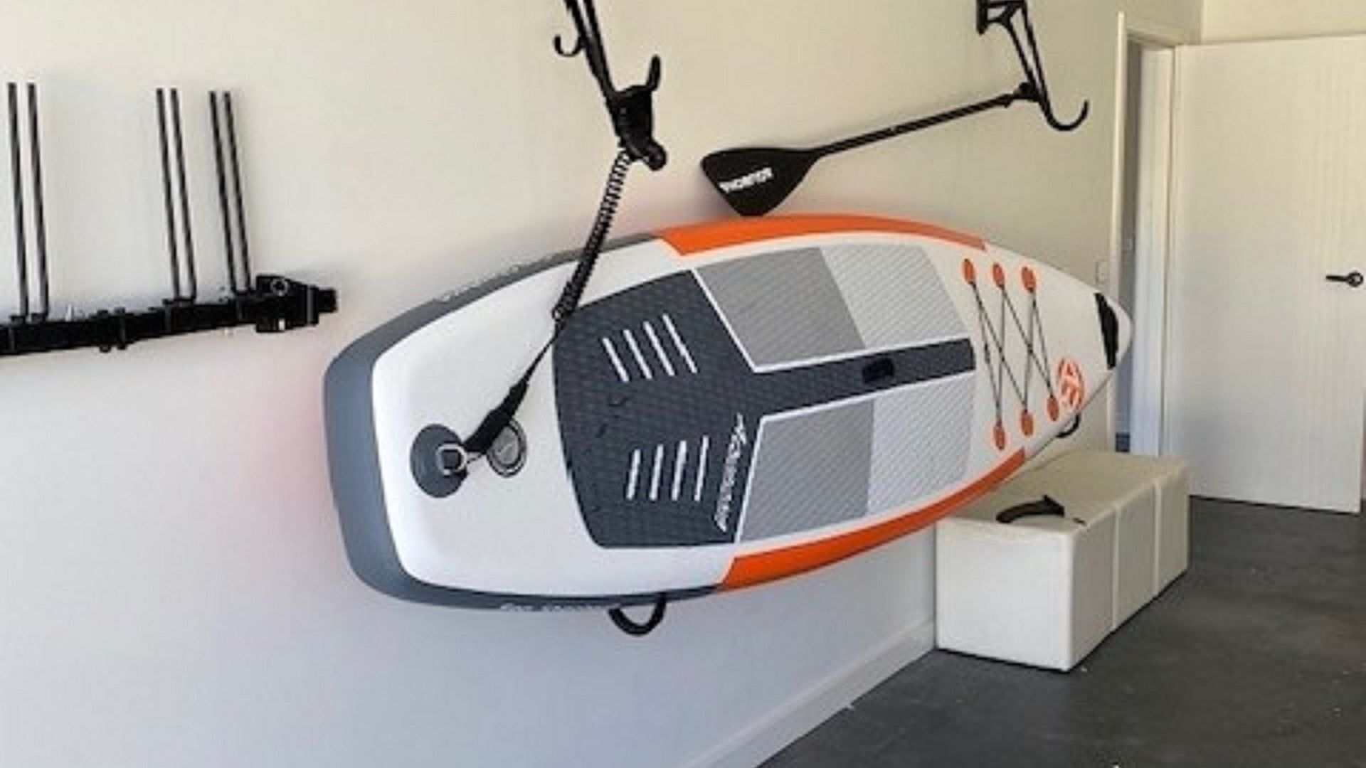 A paddleboard leaning against a wall in a room with a door and a white bench.