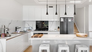 A modern kitchen with white cabinetry, a central island with stools, stainless steel appliances, and pendant lighting. - Lake Villavista - 4BR Luxury Townhouse l Pet Friendly l Lake Views l WiFi l BBQ (East Jindabyne)