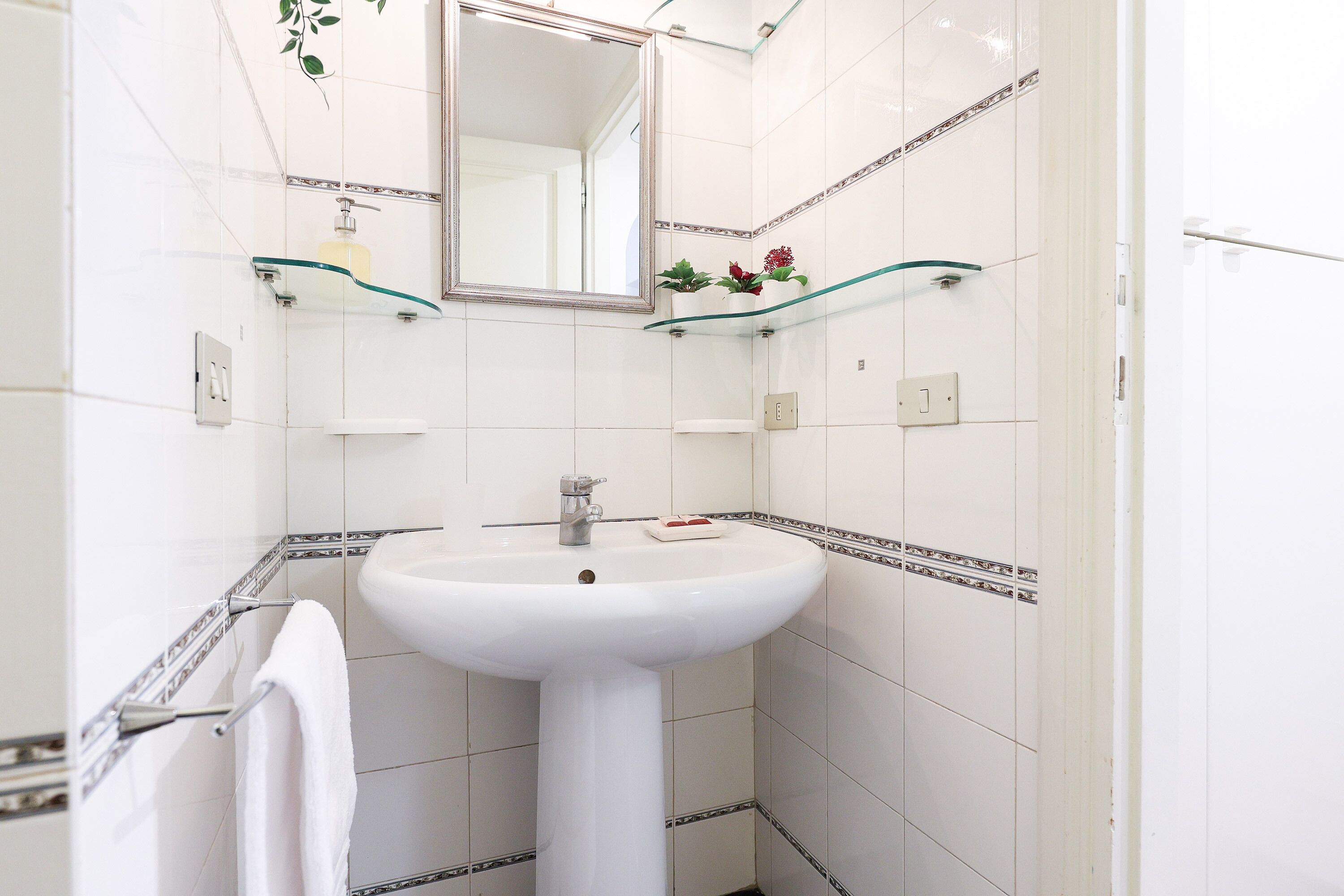 A bathroom with white tiles, a white sink, a mirror, and a towel rack.