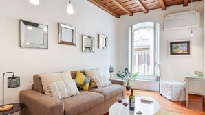 Un salon avec un canapé marron, une table basse ronde et un fauteuil blanc. Plusieurs miroirs encadrés ornent le mur, ainsi qu’une petite table d’appoint avec une lampe et une plante en pot.