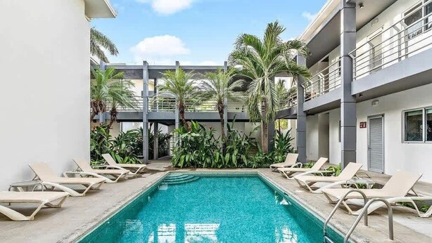Una piscina amb gandules, envoltada de palmeres i una estructura d'edifici moderna.