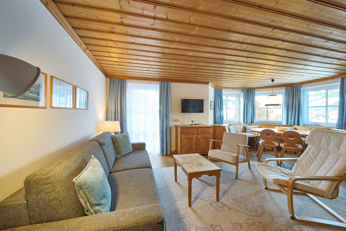 Ein gemütliches Wohnzimmer mit Holzbalkendecke, einer Couch, einem Couchtisch und einem Fernseher.