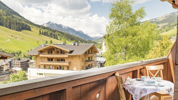 A wooden deck with a table set for dining, overlooking a mountainous landscape with buildings in the background. - Appartements Bernhofer  (Saalbach-Hinterglemm)