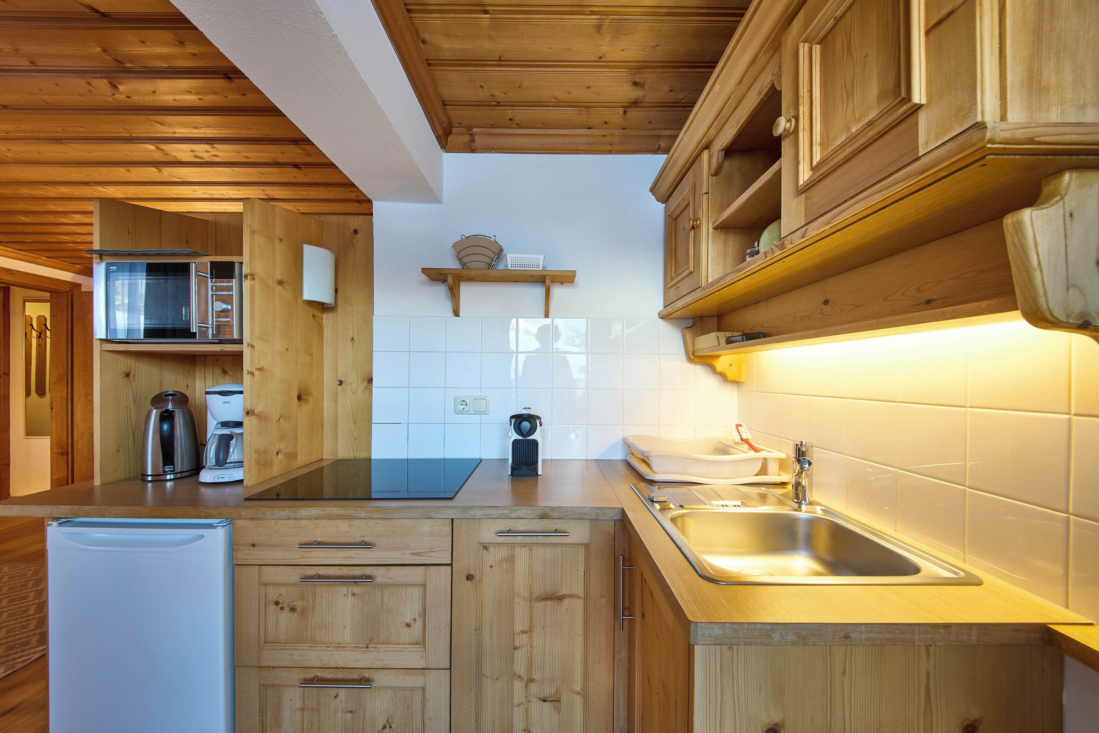 A compact kitchen with wooden cabinets, a built-in microwave, a coffee maker, and a sink.