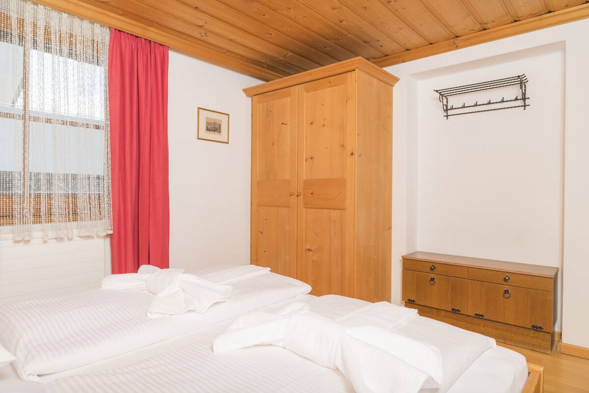 Ein Schlafzimmer mit einem Bett, einem Holzschrank und einem Fenster mit rotem Vorhang.