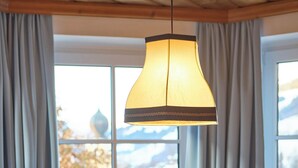 A wooden dining table with a bowl in the center, set against a window with curtains. - Appartements Bernhofer  (Saalbach-Hinterglemm)