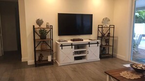 Ein Wohnzimmer mit Wand-Fernseher, einem weißen Unterhaltungsschrank mit Stauraum und einem Couchtisch aus Holz mit Dekoration.