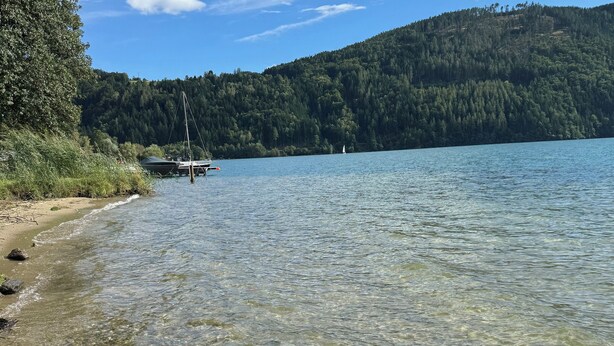 Un lac aux eaux limpides, avec un bateau amarré sur la rive, entouré de collines boisées.