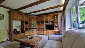Un salon traditionnel avec des meubles en bois, un téléviseur et une fenêtre donnant sur un paysage verdoyant.