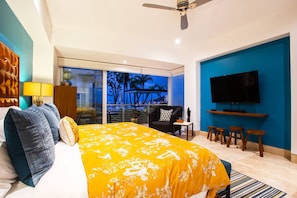 A hotel room with a large bed, a TV, a balcony with a view, and a ceiling fan.