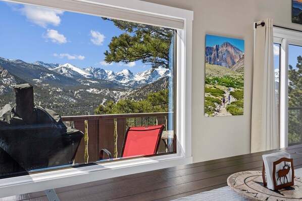 Ein Zimmer mit großem Fenster und Blick auf Berge, ein roter Sessel und ein Holztisch mit gerahmtem Bild.