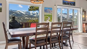 A dining area with a wooden table and chairs, large windows with mountain views, and a chandelier. - Destiny Vacation Home At Windcliff 3 Bedroom Home by RedAwning (Estes Park)
