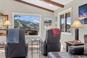 Ein Wohnzimmer mit zwei Ledersesseln, einem kleinen Tisch und einem Fenster mit Blick auf die Berge.