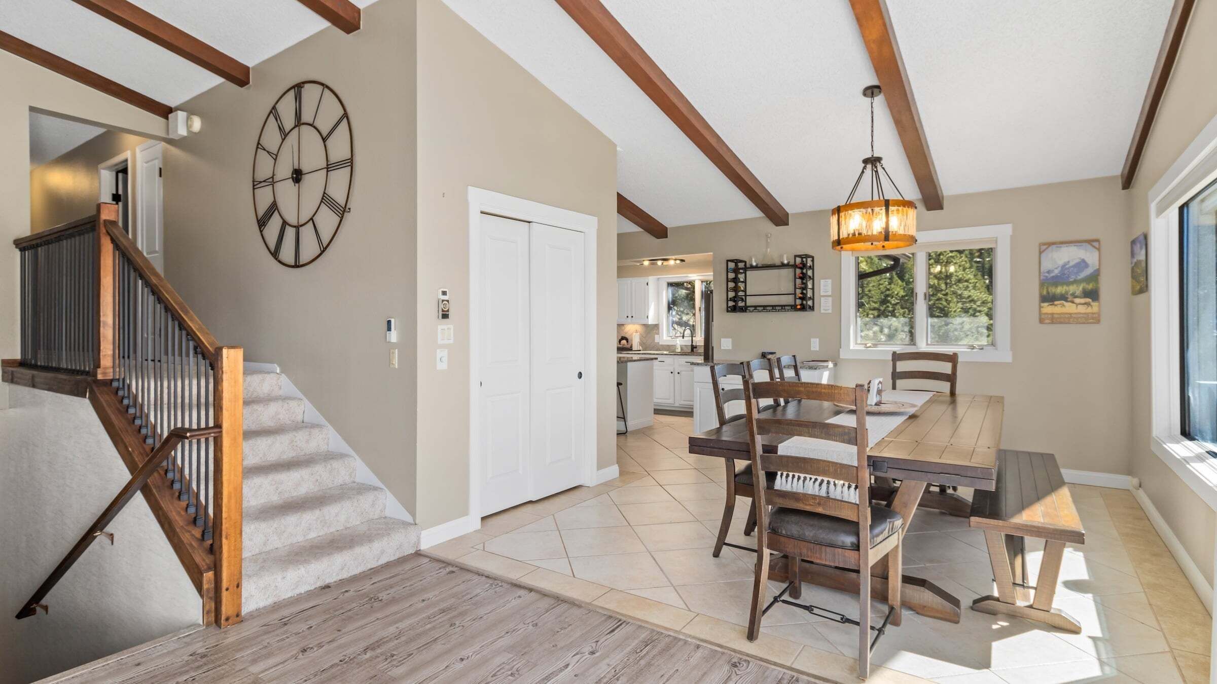 A spacious kitchen with white cabinets, a dining area with wooden chairs, a staircase with wooden railings, and a large wall clock.