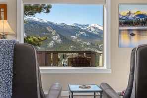 A room with a view of snow-capped mountains, a wicker basket, a glass table, and two leather chairs.