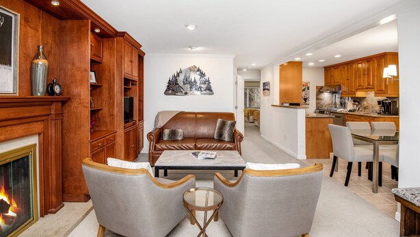 Una sala de estar moderna con chimenea, sofá de cuero y comedor con cocina al fondo.