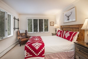 Un dormitorio con una cama grande, un cabecero de madera, una silla, una ventana con persianas y un cuadro enmarcado en la pared.