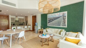 Un salon moderne avec un coin repas, une cuisine à l’arrière-plan et un mur vert à texture.