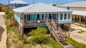 A beachfront house with a covered deck and a staircase leading to a second level.