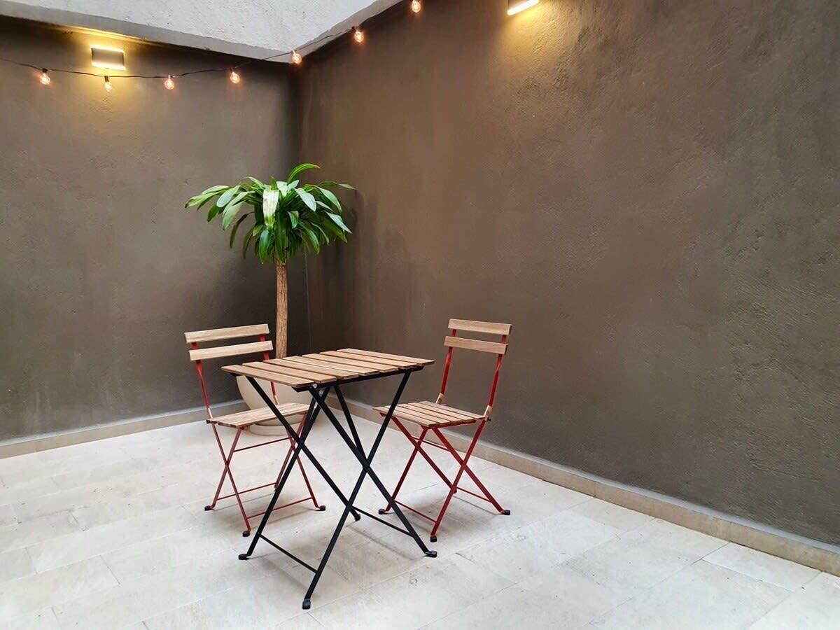 Ein kleiner Patio-Bereich mit Tisch, Stühlen, einer Topfpflanze und Lichterketten.