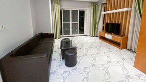 A modern living room with a sofa, a coffee table, a TV stand, and a sliding glass door leading to a balcony. - Heng Mohasal Apartment (Phnom Penh)