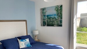 A bedroom with a bed, a nightstand, a lamp, and a window with a view of greenery. - E Villa Clara, 600m de la mer, piscine (Saint-Denis-d´Oléron)
